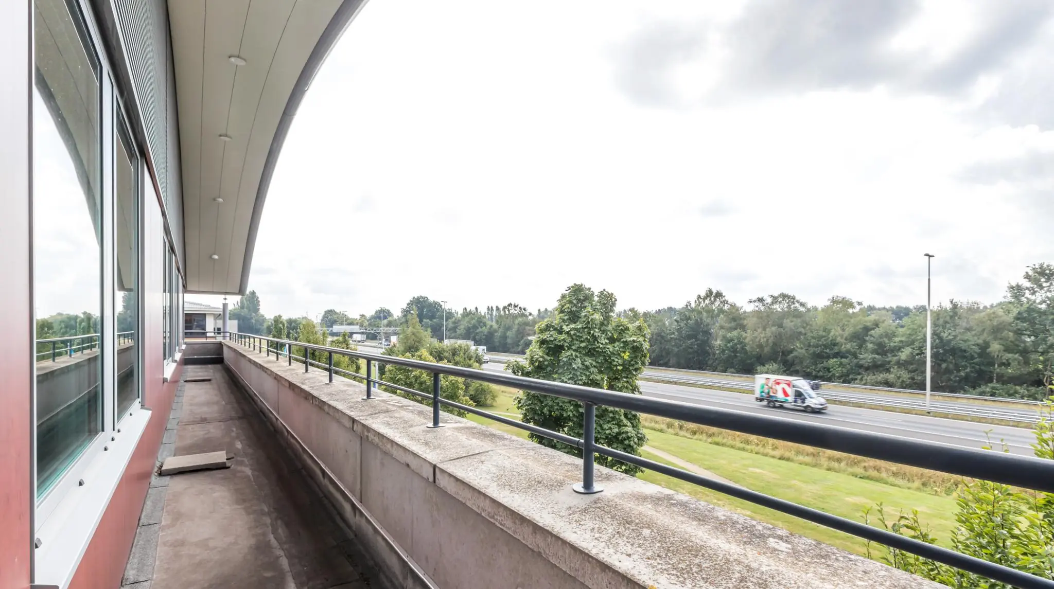 Balkon van kantoorpand De Wel met uitzicht op snelweg en omliggend groen.